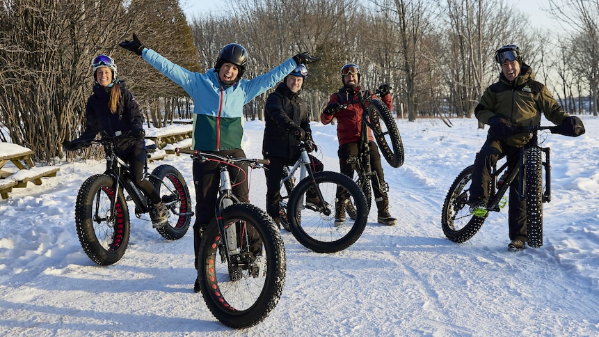 Geneviève O'Gleman accompagnée de plusieurs personnes pratiquant le vélo à pneus surdimensionnés (fatbike en anglais) en hiver.