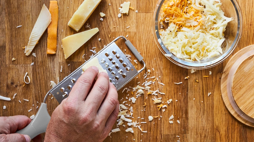 Une personne râpe plusieurs petits bouts de fromages à pâte ferme pour faire un mélange de fromages maison.