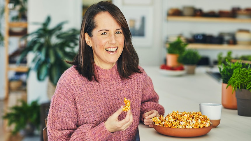 La nutritionniste Geneviève O'Gleman est assise sur une chaise au comptoir et elle tient du popcorn dans sa main.