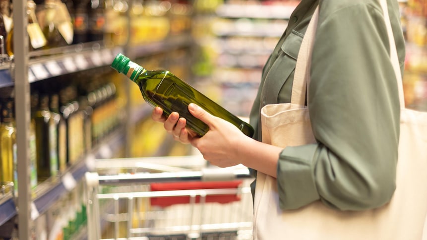 Une personne choisissant une bouteille d'huile d'olive au supermarché.