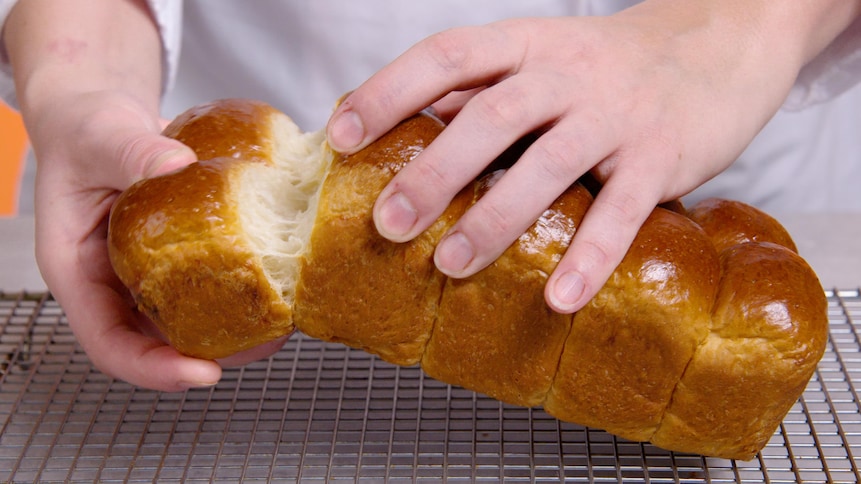 Des mains qui tiennent une miche de pain brioché.