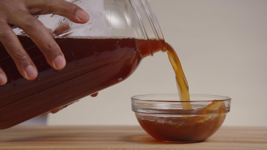 Une personne verse une boisson dans un petit bocal en verre. 