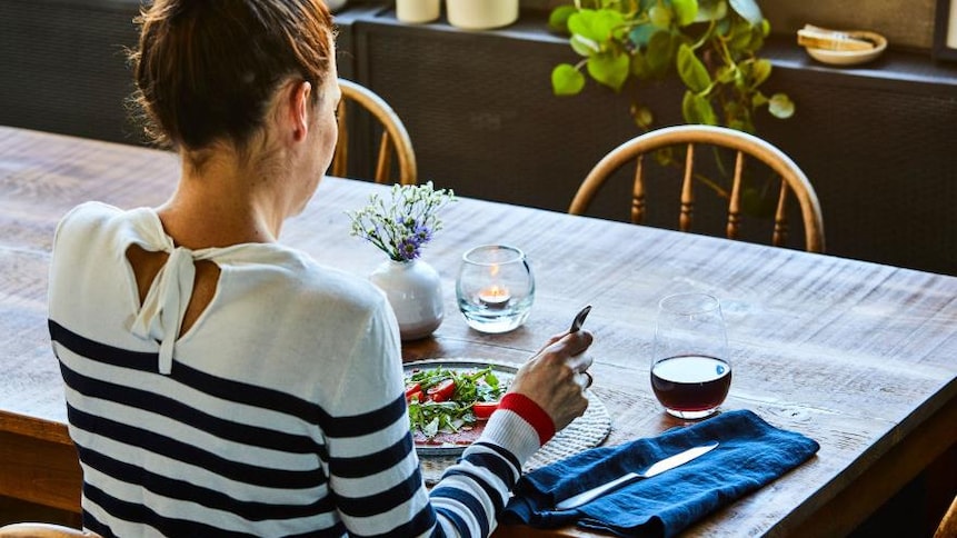 Une femme est assise à table, devant une assiette de salade.