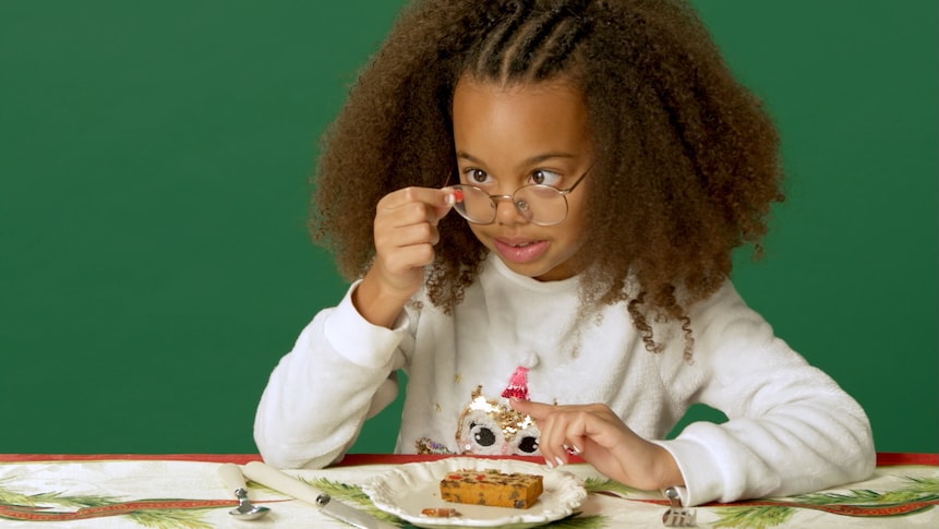 Une petite fille examine un morceau de gâteau aux fruits avant d'y gouter.