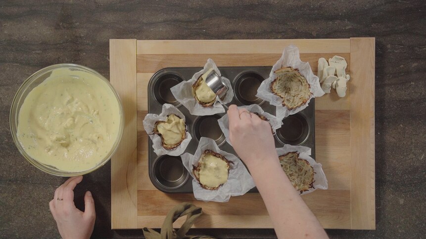 Une personne ajoute le mélange à quiche sur les croûtes.  