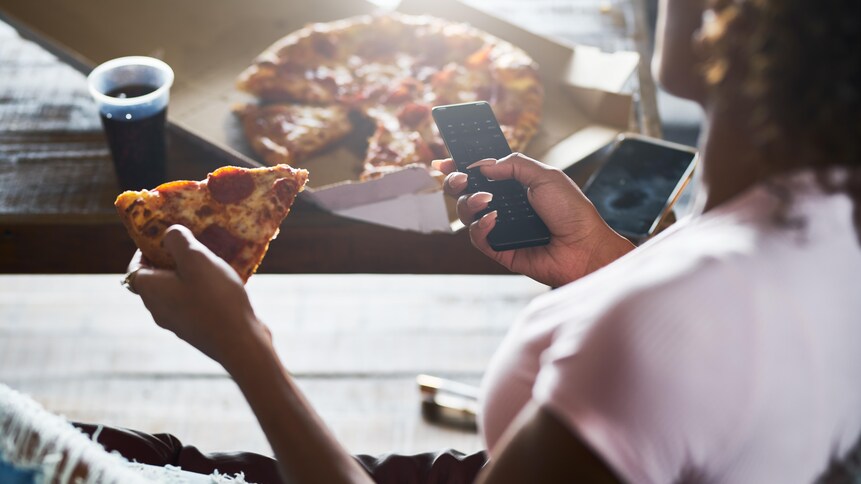 Une femme mange une pointe de pizza en regardant la télévision.