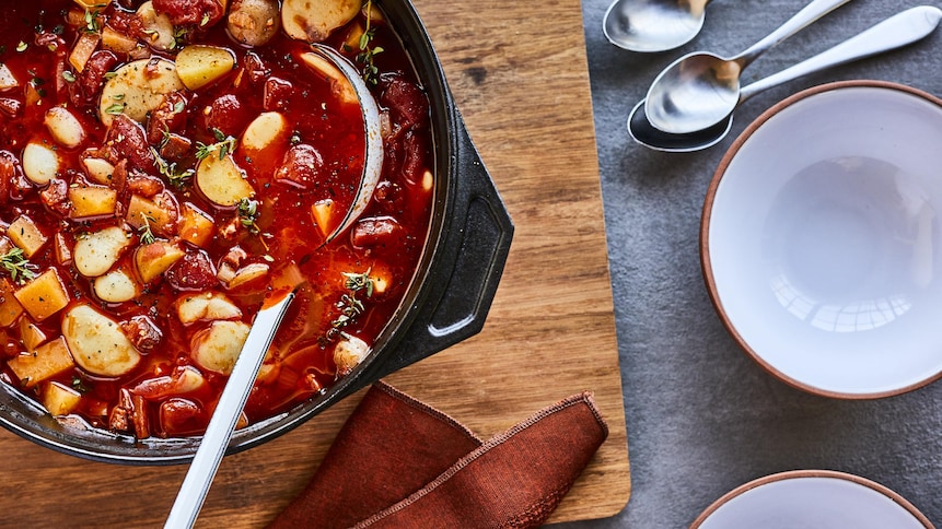 Une casserole de soupe avec une louche dedans et des bols vides à côté. 