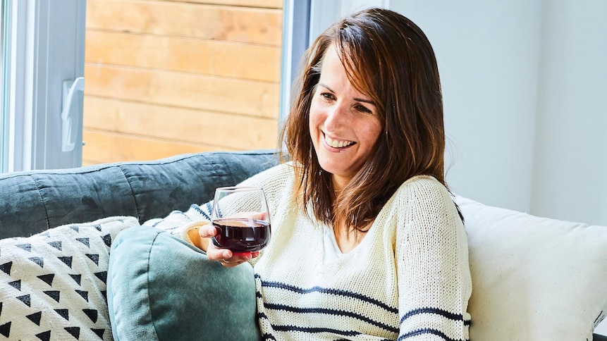 La nutritionniste Geneviève O'Gleman est assise sur un sofa, un verre de vin rouge à la main.