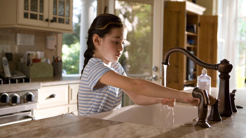 Une petite fille se lave les mains avec levier d'une cuisine. 