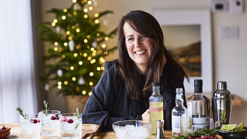 La nutritionniste Geneviève O'Gleman est assise, souriante, devant des drinks et des bouteilles de spiritueux. Elle est dans un décor de Noël.