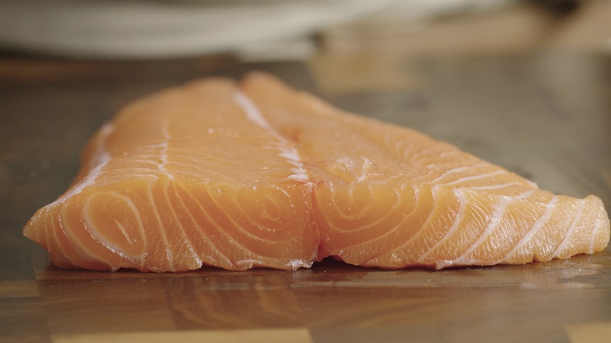 Un filet de saumon cru repose sur une planche à cuisiner. 