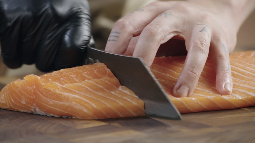 Une personne coupe le saumon pour en faire un pavé. 