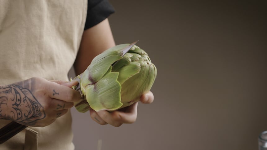 Une personne tient un couteau dans les mains et coupe le tour du légume pour retirer les feuilles. 