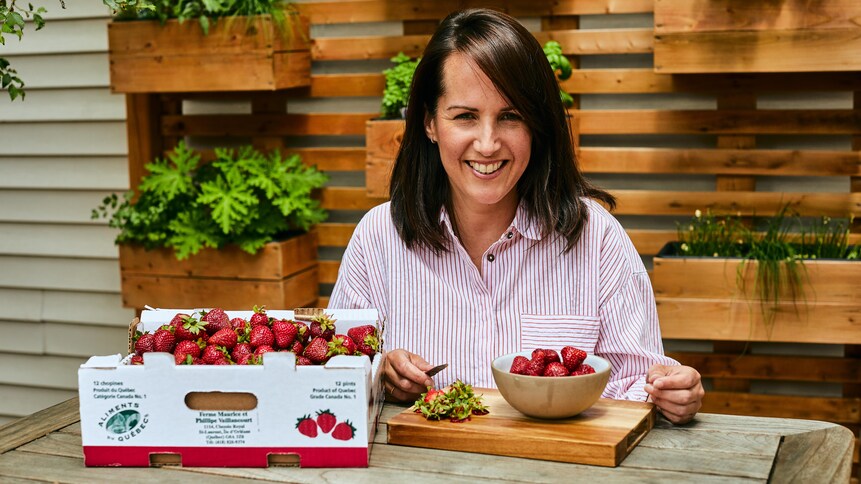 Geneviève O'Gleman est assise sur à une table à l'extérieur et elle équeute des fraises.