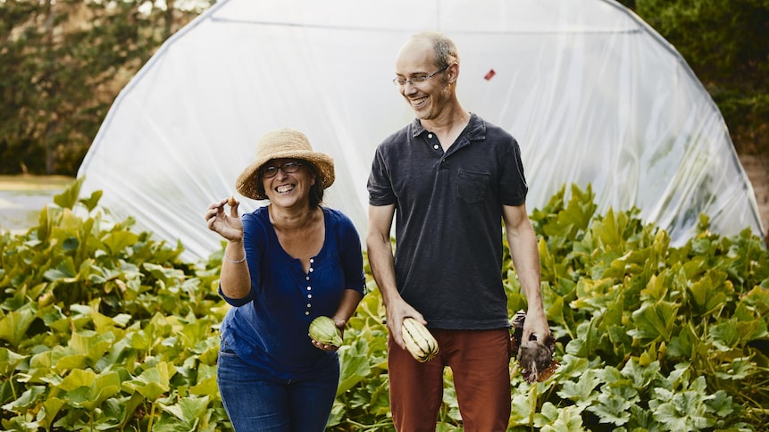 Il y a deux personnes devant une serre tenant à la main des légumes biologiques.