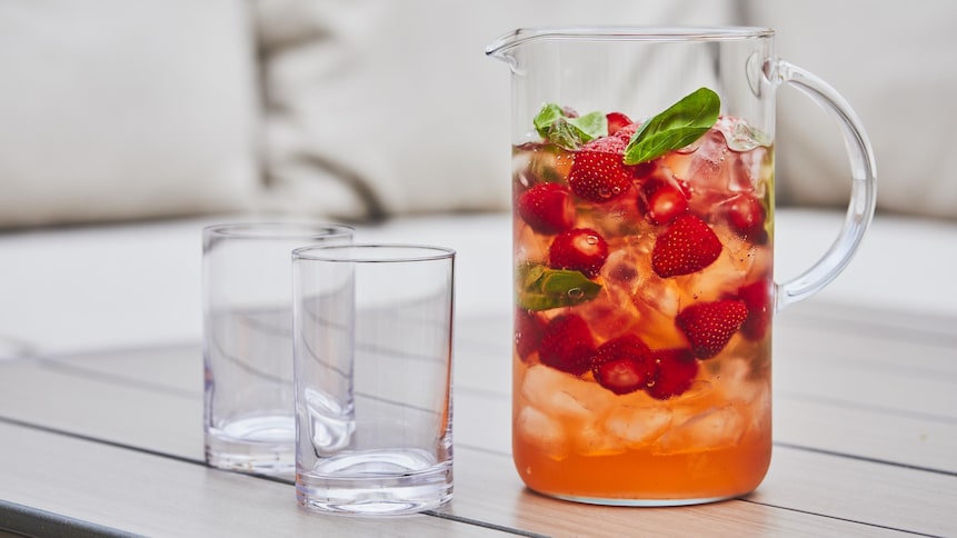 Un pichet transparent avec de l'eau fruitée aux fraises et au basilic avec deux verres vides juste à côté. 