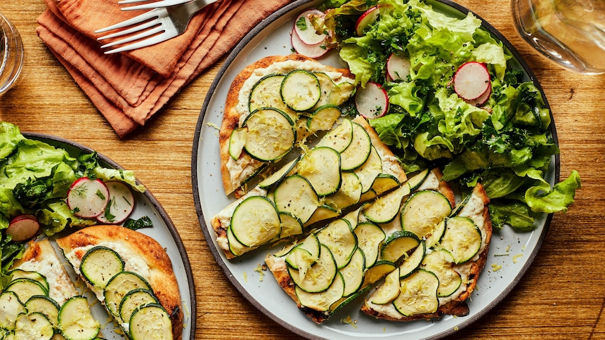 Il est possible de voir deux assiettes avec une pizza au crabe et à la ricotta dans chacunes d'elles. Il y a aussi de la salade dans chaque assiette à côté de la pizza. Les assiettes sont déposées sur une table en bois.