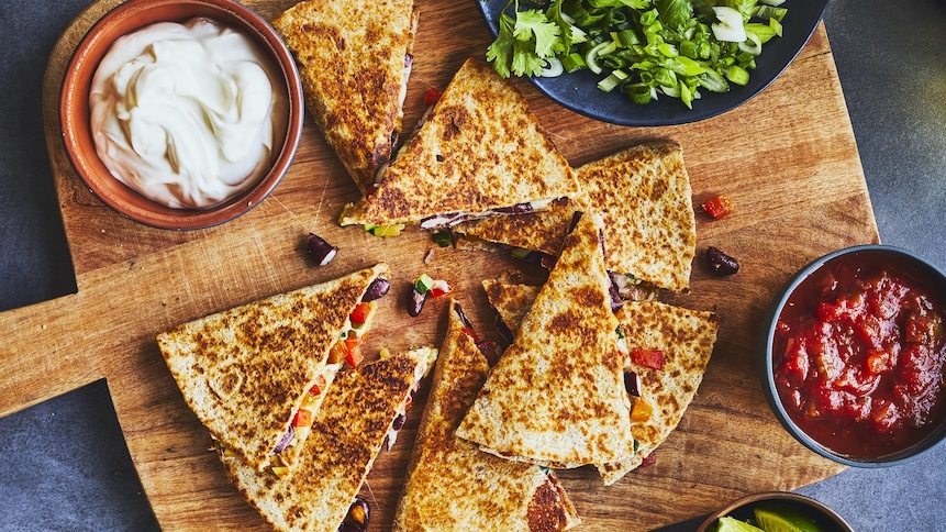 Portions de quesadillas sur une planche en bois avec un bol de salsa et de crème sure.