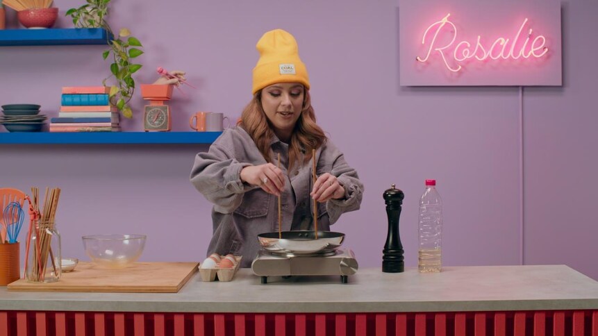 Rosalie tient deux baguettes dans un poêlon sur une plaque chauffante. 