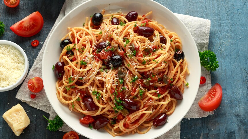 Des spaghettis recouverts de morceaux de tomates, d'olives, d'anchois et de persil.