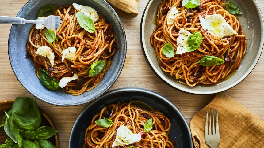 Bols de spaghetti aux tomates et au pesto posés sur une table en bois.