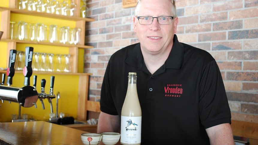 L'homme se tient derrière un bar. Une bouteille de makgeolli, un vin de riz à l'apparence laiteuse, est posée sur le bar, avec deux petits bols en céramique.