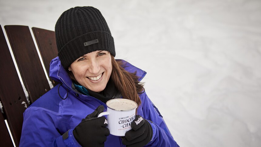 Geneviève O'Gleman boit un chocolat chaud assise sur une chaise à l'extérieur, en hiver.
