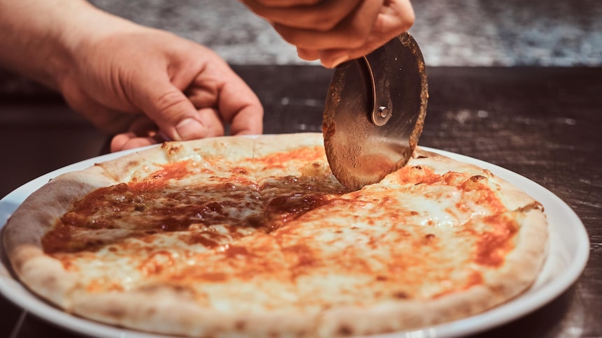 Une personne coupe une pizza margarita avec une roulette à pizza.