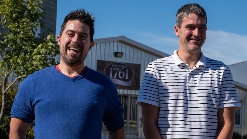 Deux frères, devant une ferme, sourient à la caméra. 