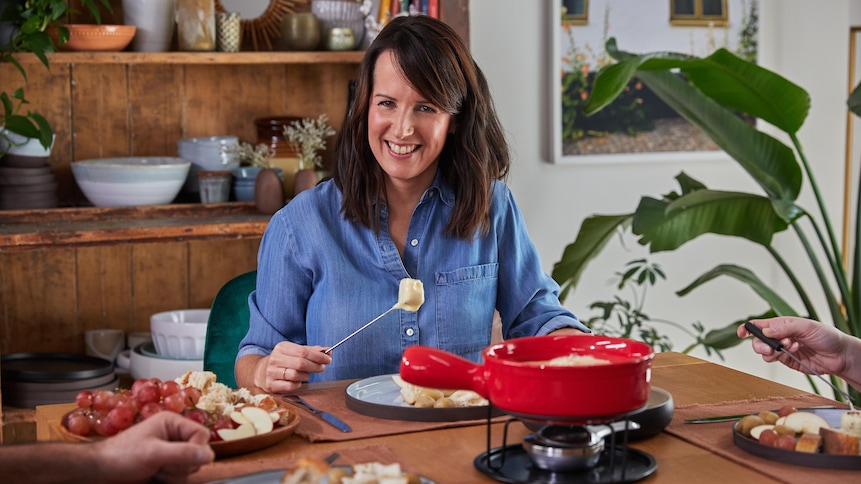 Geneviève O'Gleman est assise à la table et elle déguste une fondue au fromage avec des invités.
