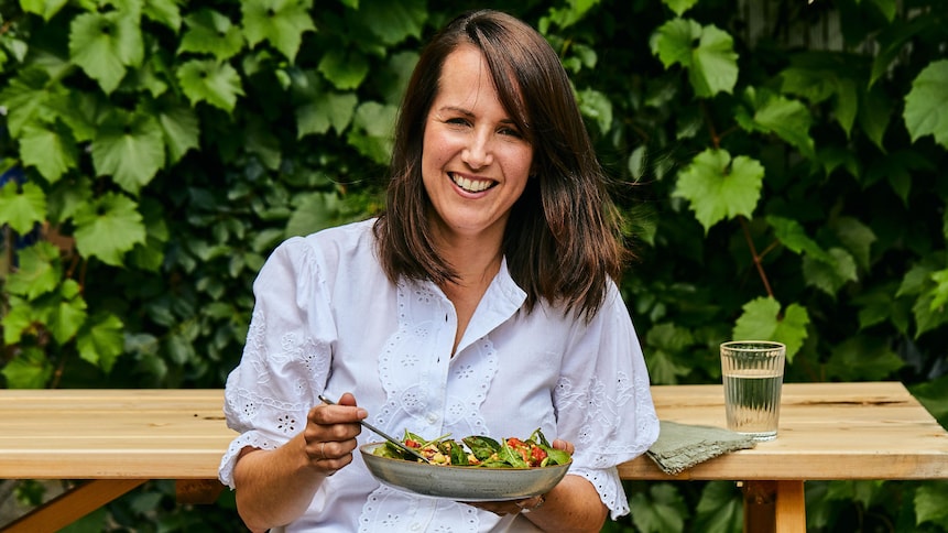 Geneviève O'Gleman est assise à une table de pique-nique et tient un bol rempli de laitue et de légumes frais.