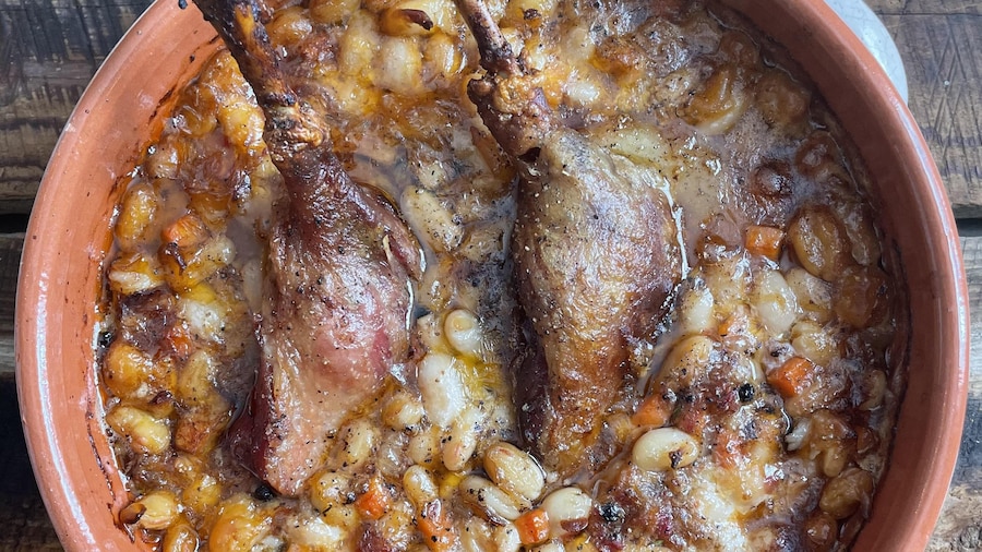 Un plat en terre cuite contenant du cassoulet composé de fèves blanches, de cuisses de canard confites, de saucisse de Toulouse et de lard fumé.