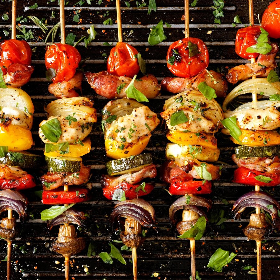 Des brochettes de légumes et de viande, sur lesquelles on a saupoudré des épices et des herbes, cuisent sur une grille de barbecue.