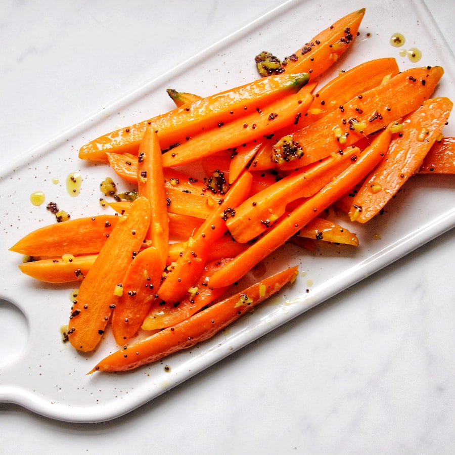Des carottes glacées au gingembre, graines de moutarde et au miel déposées sur un plateau.