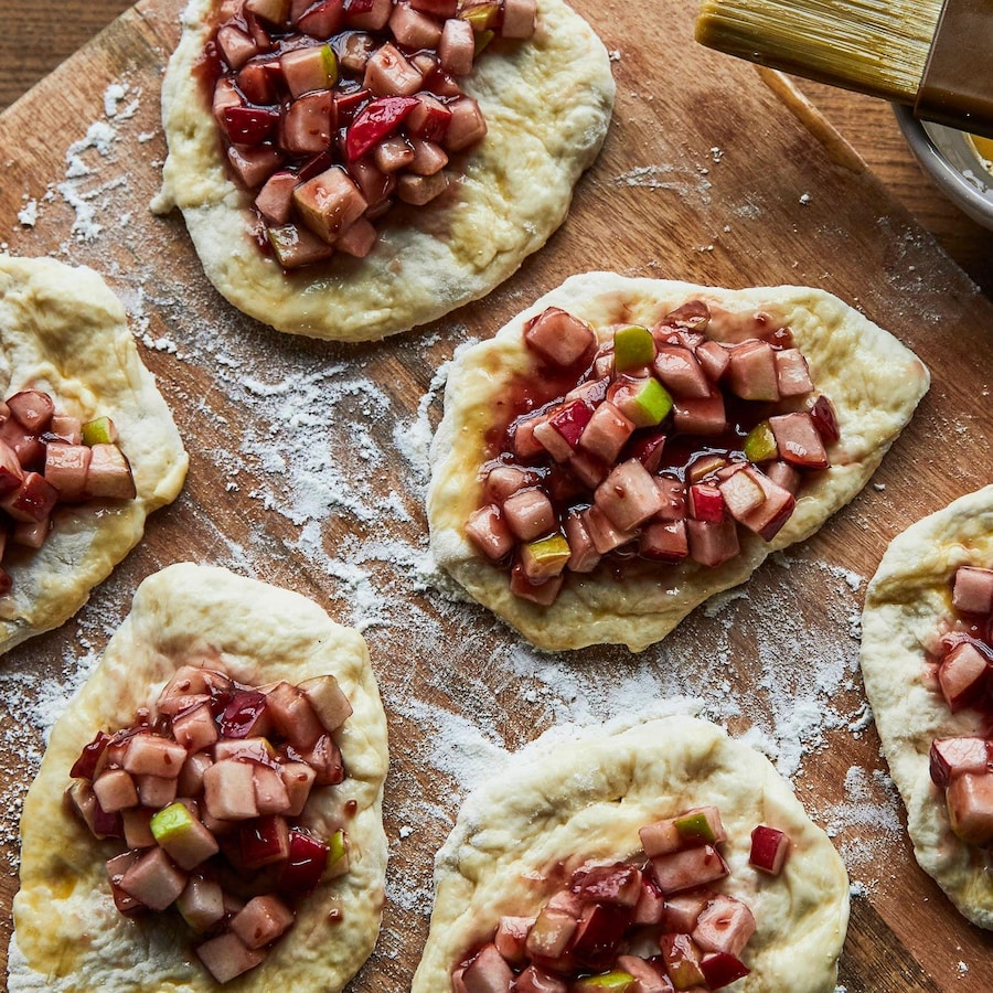 Sur une planche de bois, de la pâte à chausson été roulé et coupé en quatre morceaux. Sur chacune des pâtes des quartiers de pomme et un coulis de petits fruits ont été déposés.
