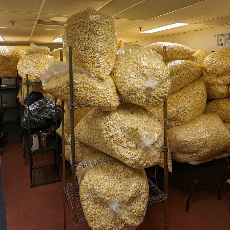Des grands sacs transparents remplis de maïs soufflé sont empilés sur des étagères dans une grande salle de rangement.