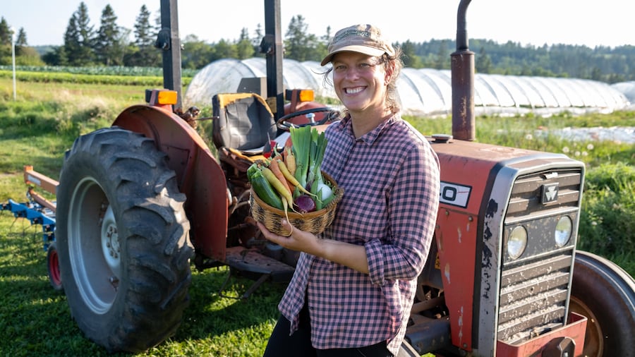 Un dame tenant un panier de légumes devant un tracteur.