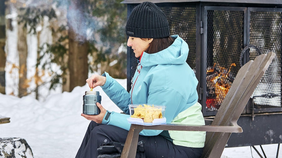 Geneviève O'Gleman est assise sur une chaise dehors dans un contexte de sport d'hiver et mange des nachos.