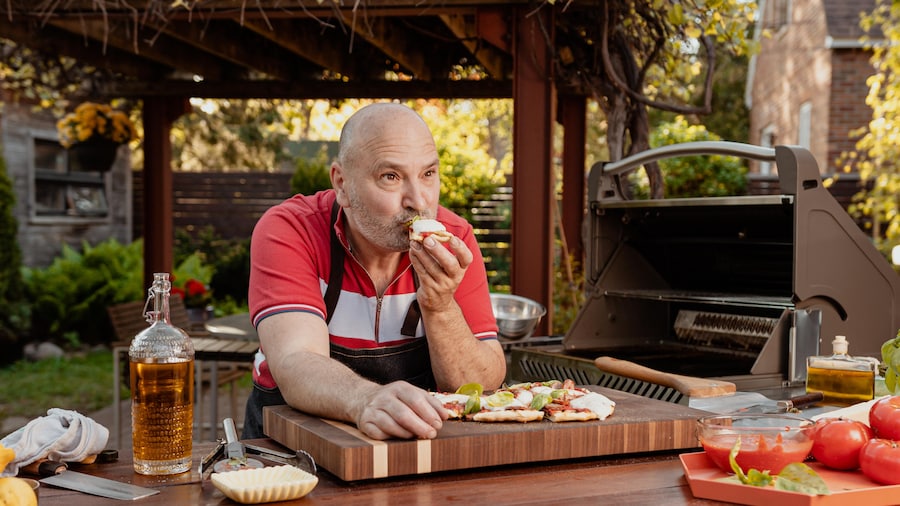 Le chef Marc Maulà dans une cuisine extérieure qui déguste un morceau de pizza.