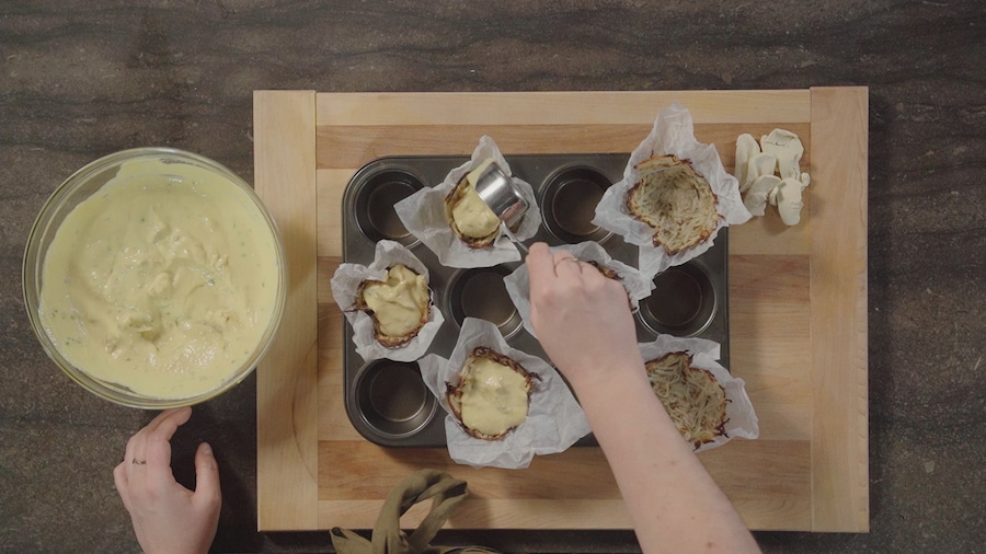 Une personne ajoute le mélange à quiche sur les croûtes.  