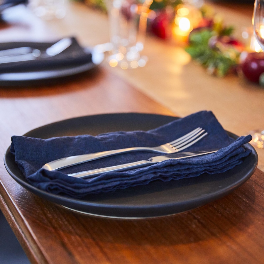 Assiette foncée avec serviette en tissu bleu et couvert sur le dessus.