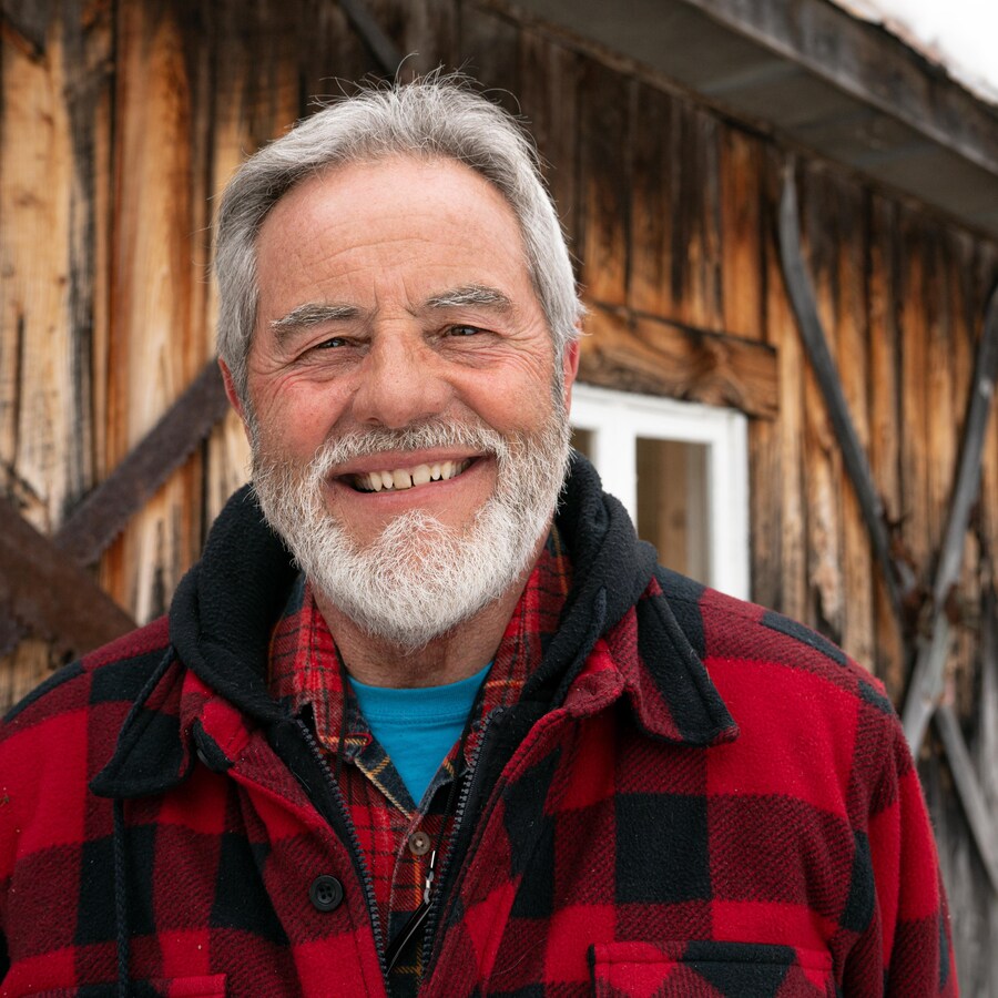 André Pollender sourit devant sa cabane en bois.