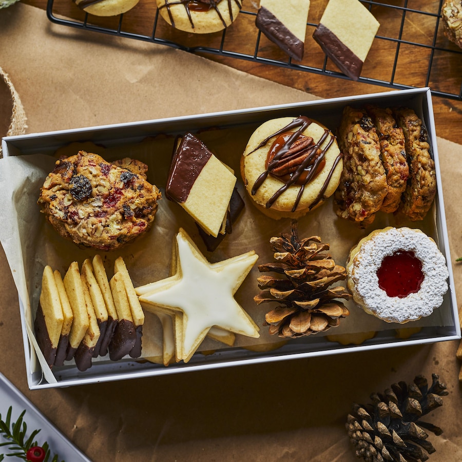 Une variété de biscuits de Noël disposés dans une boîte blanche entourée de rubans et de décorations de Noël. 