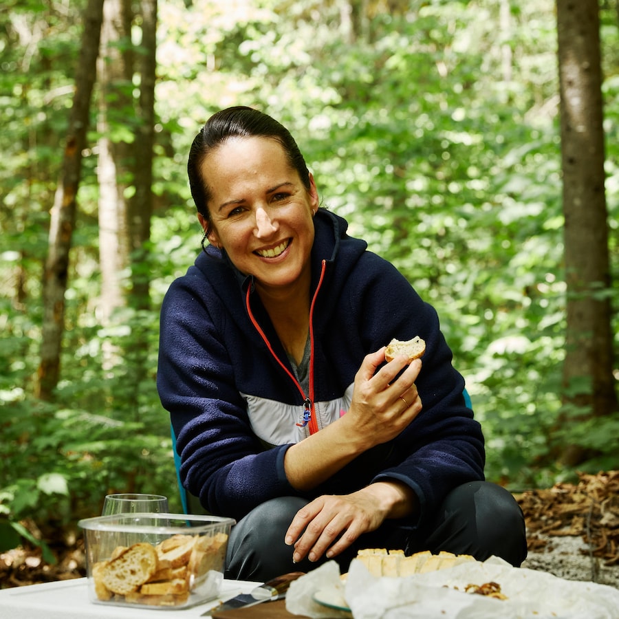 Geneviève O'Gleman en camping qui déguste des croutons de pain avec un fromage cuisiné sur un feu de camp.