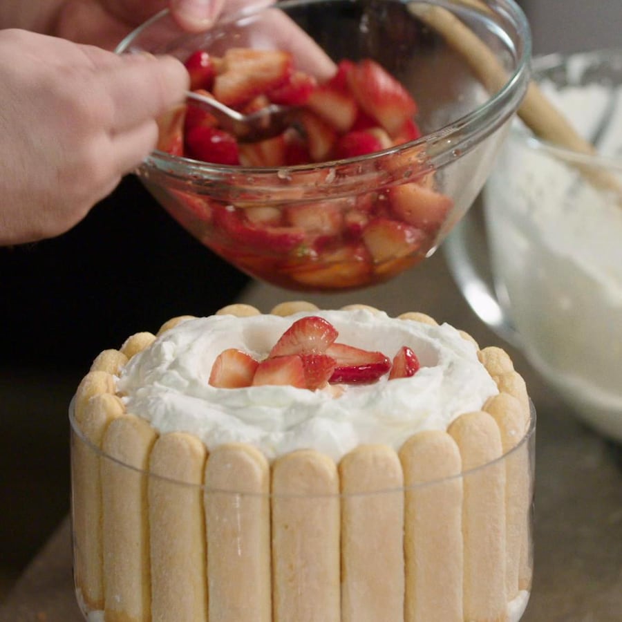 Une personne dépose des fraises sur un gâteau garni de crème fouettée.