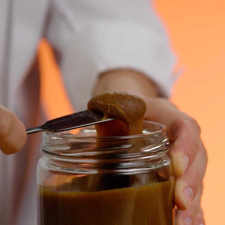 Un couteau rempli de caramel au dessus d'un pot en verre. 