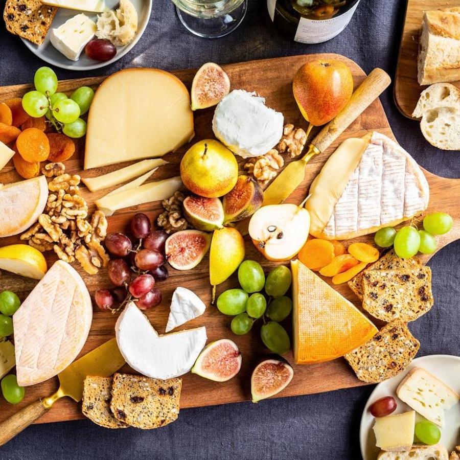 Plateau de plusieurs fromages fins avec des noix, des fruits et des craquelins.