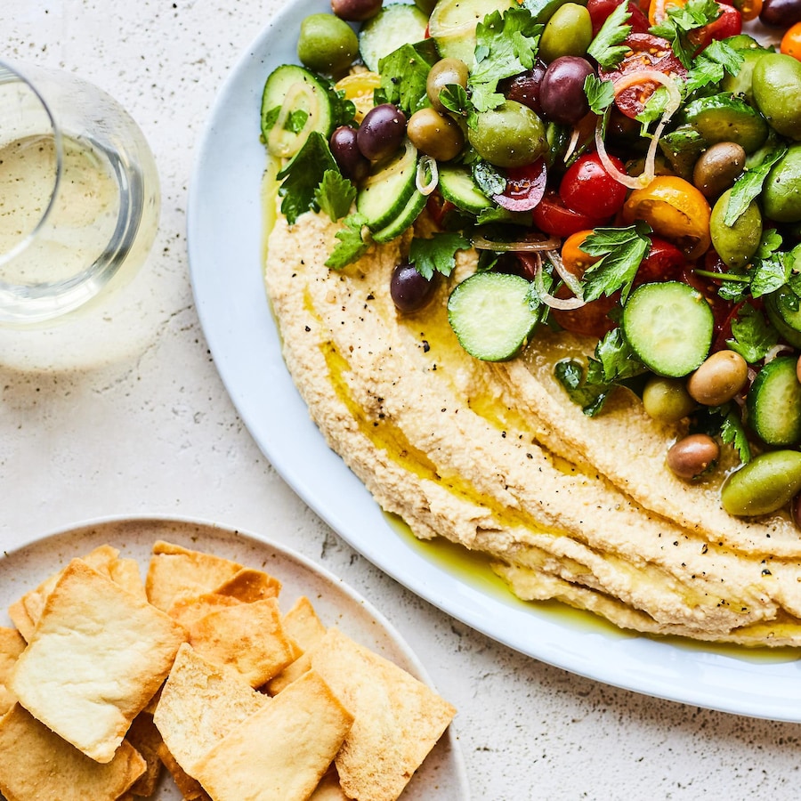 Assiette d'houmous garni d'olives, de tomates, de concombres et de persil.