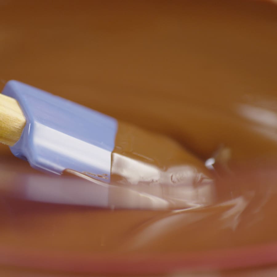Une personne touille doucement une sauce au chocolat avec une spatule souple. 