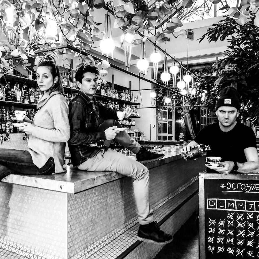 Trois personnes, dont deux sur un comptoir, regardent la caméra dans cette photo en noir et blanc.